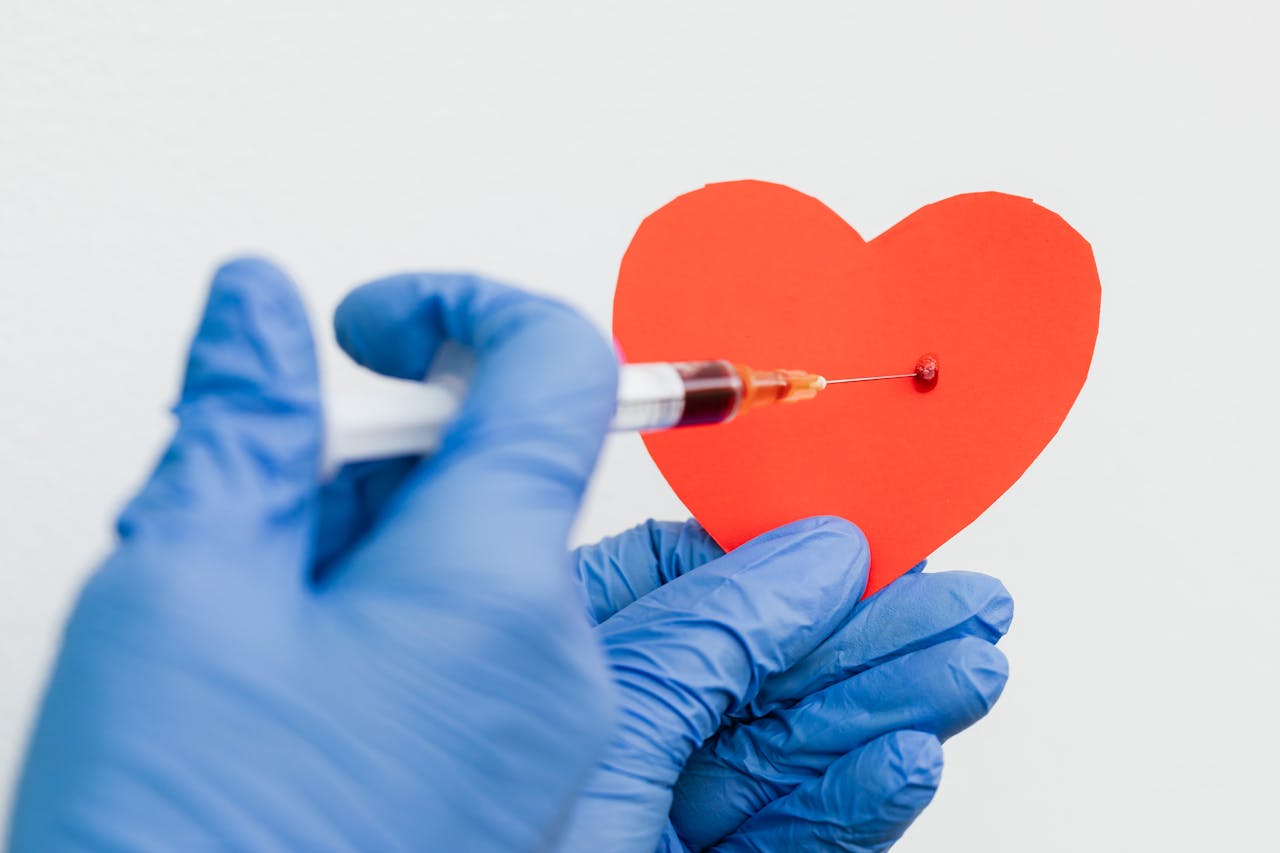A conceptual image of a syringe injecting a red paper heart held by gloved hands, symbolizing health or love.